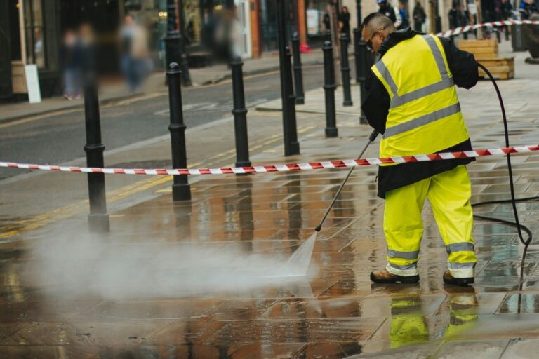 Worker in hi-vis gear pressure washing wet paving stones with a spray lance
